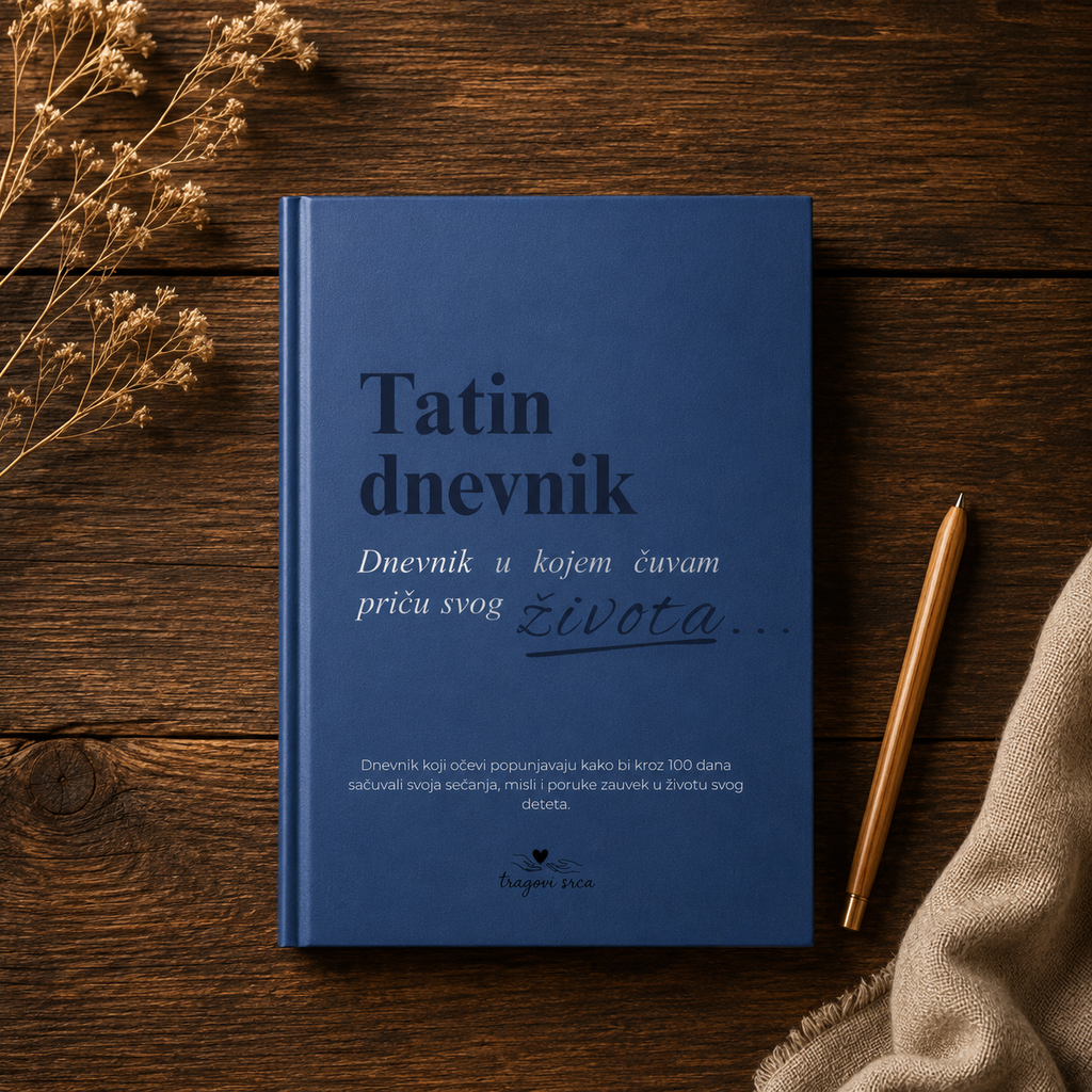 A blue hardcover journal titled 'Tatin dnevnik' lies on a dark wooden surface, styled with dried flowers, a gold pen, and a beige fabric corner.